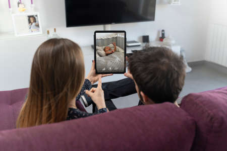 Two parents sitting on the sofa and monitoring their baby on the tablet