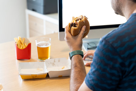 Man eating fast food while working in his office in front of the computerの写真素材