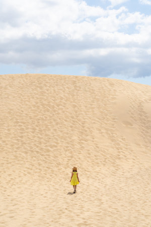 Girl in a yellow dress in the middle of a mountain of sand in a desertの写真素材