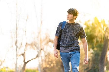 Young man with a bag walking around the park with some trees on the backgroundの写真素材
