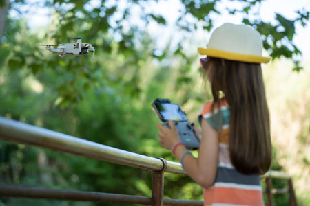 Little girl flying a small drone in the park with a remote controller
