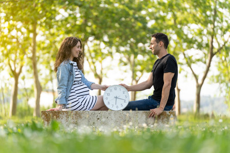 Couple with pregnant woman sitting with a clock in the parkの写真素材