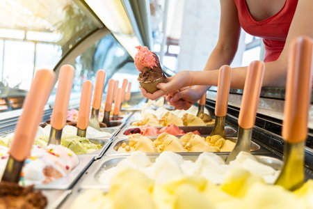 Ice cream showcase with a saleswoman preparing a tub with two flavorsの写真素材