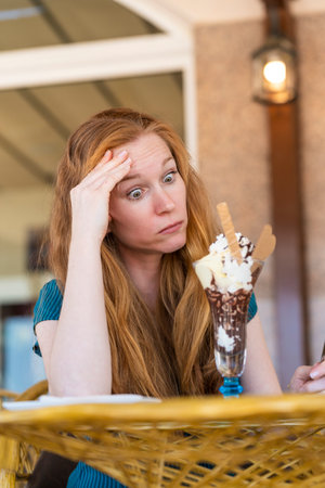 Surprised woman having a glass of ice cream on a terrace of an ice cream parlorの写真素材