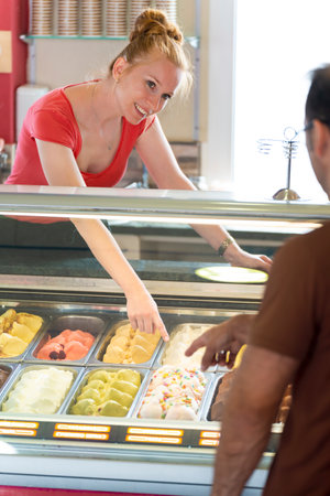 Man choosing a flavor of ice cream in a store with a female assistantの写真素材