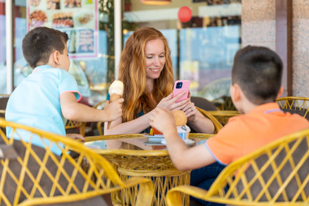 Mother on a terrace of a coffee shop with her two children looking her phoneの写真素材