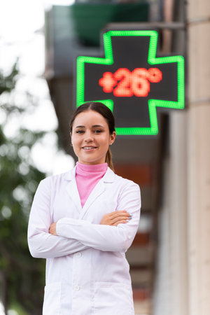Young female pharmacist in front of a pharmacy cross in the streetの写真素材