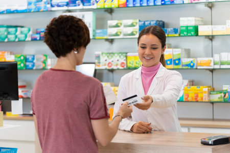 Customer gives a health insurance card to a young pharmacist inside the pharmacyの写真素材