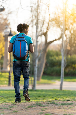 Young black student with a bag walking around the parkの写真素材