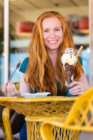 Redhead woman having a glass of ice cream on a terrace of an ice cream parlorの写真素材