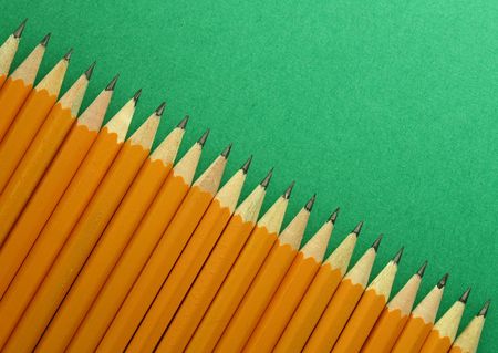 several yellow pencils aligned side by side over a green background