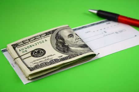  Several folded hundred dollar bills over a check and a pen on a green surface