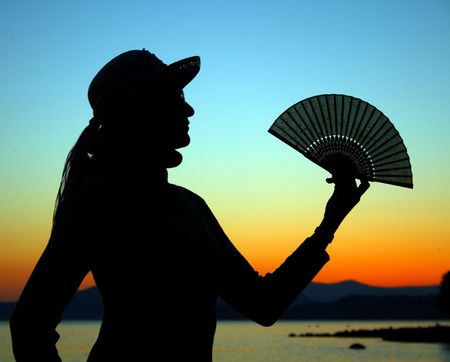 silhouette of a woman with a hat and holding a japanese folding fanの写真素材