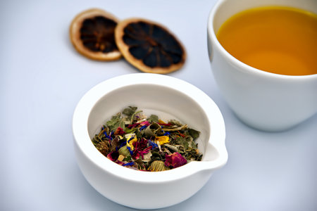 Dried flower petals in a mortar, a cup of tea and dried orange slices against a white backgroundの写真素材