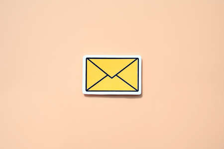 Yellow message sign or envelope icon against a salmon-colored backgroundの写真素材