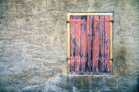Weathered facade of an abandoned building with window and closed shuttersの写真素材