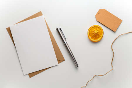 Christmas greeting card with craft envelope gift tag, fountain pen and a slice of dried orange on a clean white desk. Table top view, flat lay, copy space.の写真素材