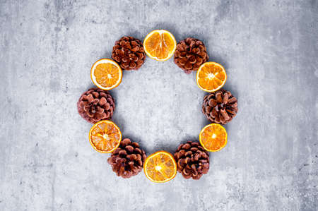 Modern Christmas wreath or Advent crown in bright colors: dried orange slices alternating with pine cones against a concrete-colored background. Table top view, flat lay, copy space.の写真素材