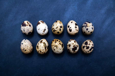 Ten typical patterned quail eggs (with a little gold dust) in two rows on a dark slate serving plate. Table top view of a kitchen, restaurant, or cooking scene.の写真素材