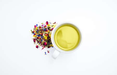 Taking a tea break: Dried herbal tea leaves next to a cup of hot, freshly brewed tea on a white background. Table top view, flat lay, copy space.の写真素材