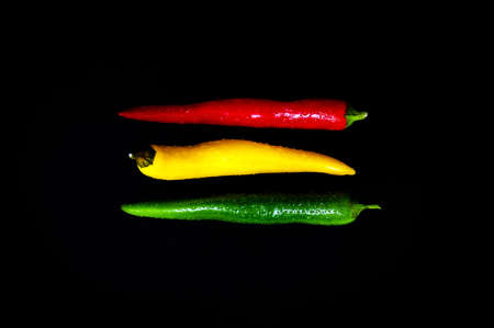 Coalition in red, yellow and green: Spicy threesome of fresh chilli pods against black background. Table top view, flat lay, copy space.の写真素材