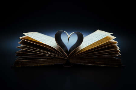 Music is the literature of the heart. Opened, antiquarian book (19th century) with sheet music and pages curved into a heart shape on black background.の写真素材