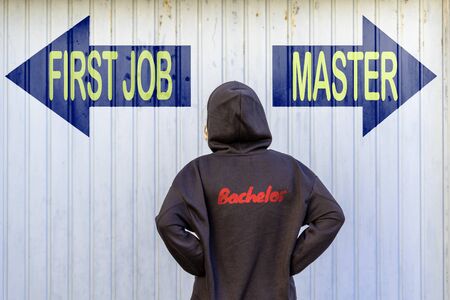 A female bachelor graduate in front of two blue guideposts with yellow text FIRST JOB and MASTERの写真素材