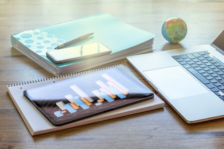 A laptop, mobile phone and tablet with a bar chart on a wooden desk at homeの写真素材