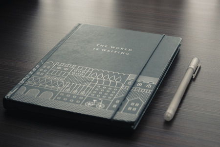 Travel journal and pen placed on a dark wood tableの写真素材