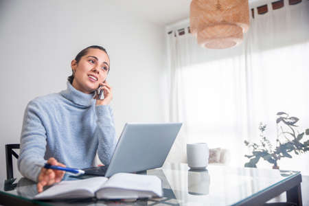 businesswoman telecommuting at home with her computer, mobile and agenda at home.の写真素材