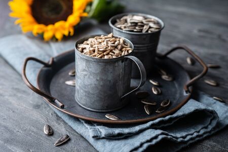 Healthy snack, a heap of whole and peeled sunflower seeds in jars on stone backgroundの写真素材