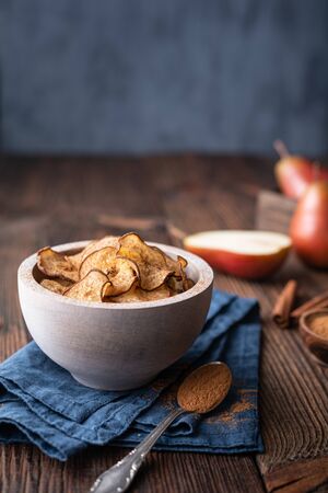 Sweet delicious snack, homemade oven dried crispy pear chips sprinkled with cinnamon on rustic wooden backgroundの写真素材