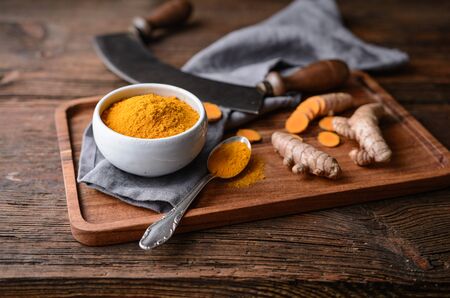 Anti-inflammatory food ingredient, turmeric powder in a ceramic bowl and fresh root on rustic wooden backgroundの写真素材