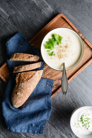 Delicious creamy celery soup topped with black pepper and fresh leaves, served with crusty bread, on rustic stone backgroundの写真素材
