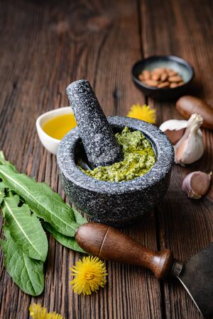 Healthy dandelion pesto with almonds, garlic, olive oil and Parmesan cheese in a stone mortar on rustic wooden backgroundの写真素材