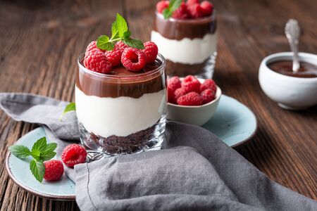 Delicious layered dessert with cream cheese, crushed chocolate cookies, topped with ganache and fresh raspberries in a jarの写真素材