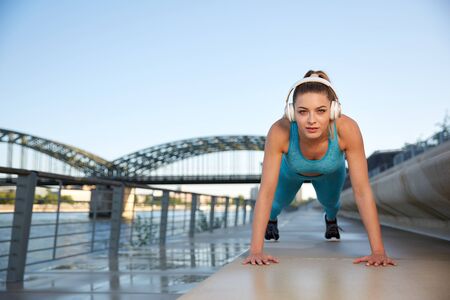 Early in the morning, after sunrise, in the city by the river, a young attractive woman does fitness...