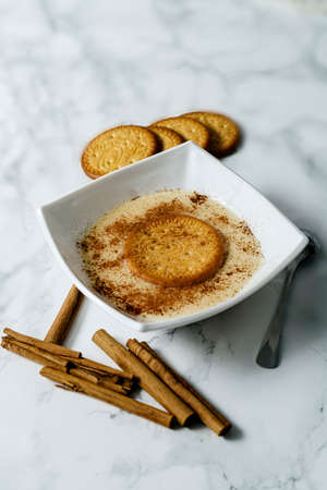 Bowl of custard cream with biscuit and cinnamon