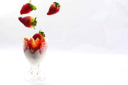 Strawberries falling into glass cup with cream on white backgroundの写真素材