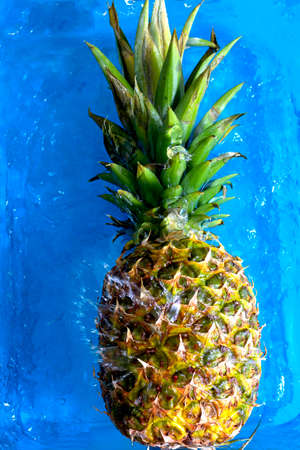 Pineapple falling into water and splashing on blue background