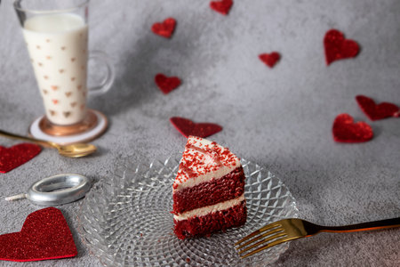 red velvet cake with red hearts and glass of milk on stone gray background with gold cutlery