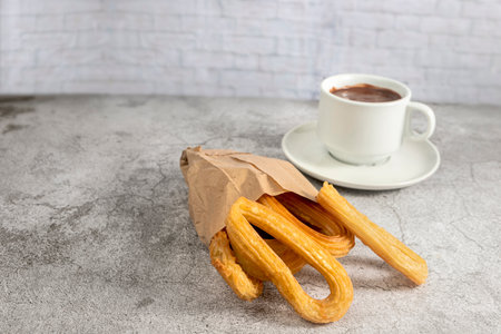 Churros in paper bag with cup of hot chocolate, typical spanish breakfast, on stone gray backgroundの写真素材