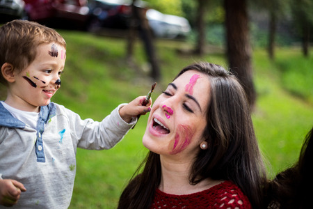 Happy child painting his mother´s face in the park.