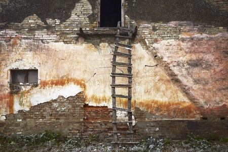 Old weathered ladder leaning on the facade of the old dilapidated run-down farmhouse.の写真素材