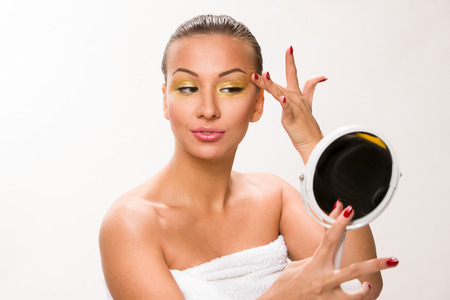 Gold make up. Brown sleek hair beautiful woman looking at mirror.の写真素材