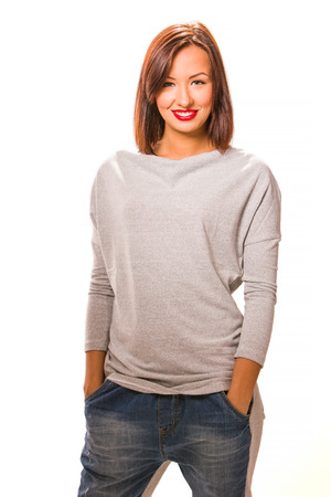 Beautiful happy young woman standing with hands in pockets, wearing jeans and grey blouse.の写真素材