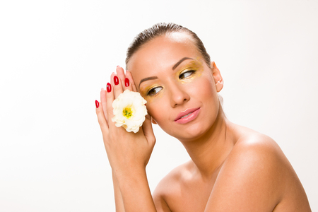 Gold make up. Brown sleek hair beautiful woman with white flower in hands close to face.の写真素材