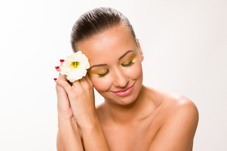 Gold make up. Brown sleek hair beautiful woman with white flower in hands close to face.の写真素材