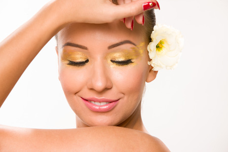 Gold make up. Brown sleek hair beautiful woman with white flower in behiond ear.の写真素材