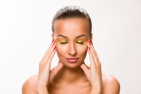 Gold make up. Brown sleek hair beautiful woman with hands on temples.の写真素材